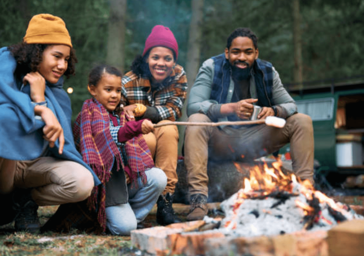 essential gear for camping with kids featured image - family around a campfire roasting marshmallows